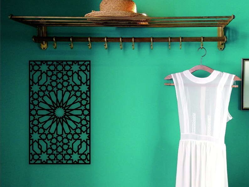May include: A black metal wall decor with a geometric pattern of stars and circles. The decor is hanging on a teal wall with a brass shelf and hooks above it. A white dress is hanging on a wooden hanger on the hooks.