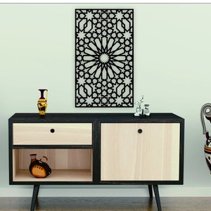 May include: A wooden cabinet with two drawers and a shelf. The cabinet is light wood with black trim. There is a black metal wall decor with a geometric pattern above the cabinet. There are two small vases on the top of the cabinet, one is brown and the other is gold. There is a large vase with a black and white pattern on the right side of the cabinet.