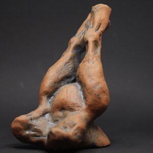 May include: A handcrafted, abstract ceramic sculpture in shades of brown and blue. The organic form has a textured surface and appears to be a stylized representation of two figures intertwined. The sculpture is set against a dark background.