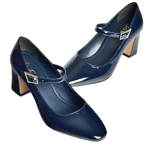 May include: A pair of navy blue patent leather Mary Jane heels. The shoes have a rounded toe, a strap across the top with a decorative buckle, and a block heel with a gold-colored base. The heels are approximately 2.5 inches high.