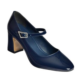 May include: Navy blue patent leather Mary Jane style shoe with a square toe and a block heel. The shoe features a strap across the top of the foot with a rhinestone buckle. The heel is approximately 3 inches high.