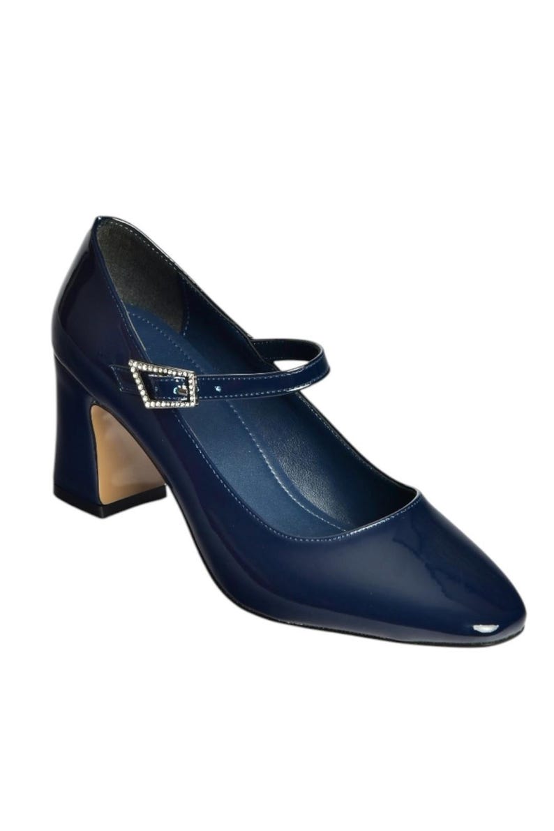 May include: Navy blue patent leather Mary Jane style shoe with a square toe and a block heel. The shoe features a strap across the top of the foot with a rhinestone buckle. The heel is approximately 3 inches high.