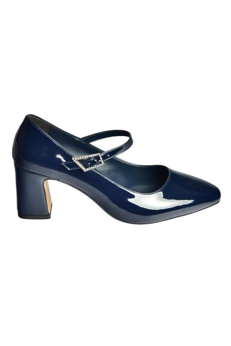 May include: Navy blue patent leather Mary Jane style shoe with a square toe and a block heel. The shoe features a strap across the top of the foot with a decorative buckle. The heel height is approximately 2.5 inches.
