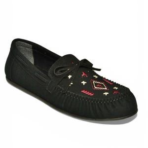 Może przedstawiać: Czarne zamszowe mokasyny z ozdobnymi przeszyciami i kokardą. Cholewka posiada geometryczny wzór w kolorze czerwonym i białym. Podeszwa jest w ciemniejszym odcieniu czerni. Wygodna i stylowa opcja obuwia.