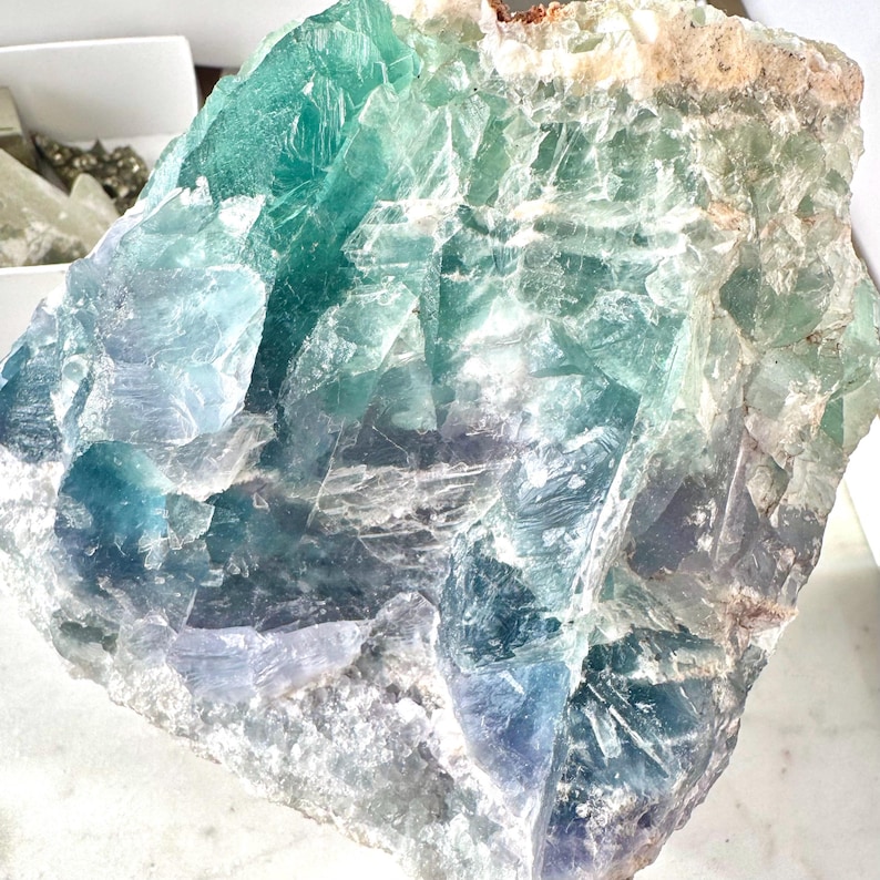 May include: A large, rough-hewn piece of fluorite crystal with a mix of green, blue, and white colors. The crystal has a natural, unpolished look.