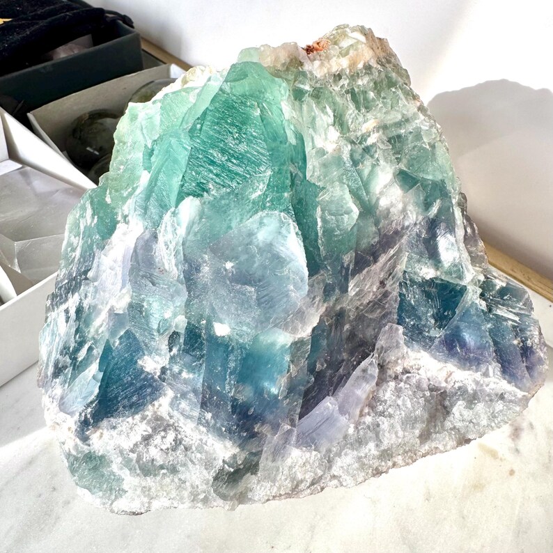 May include: A large, rough-hewn fluorite crystal with a mix of green, blue, and white hues. The crystal has a natural, unpolished appearance.