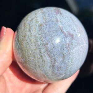 May include: A polished, grey and white agate sphere with gold flecks and swirling patterns. The sphere is smooth and has a high gloss finish.