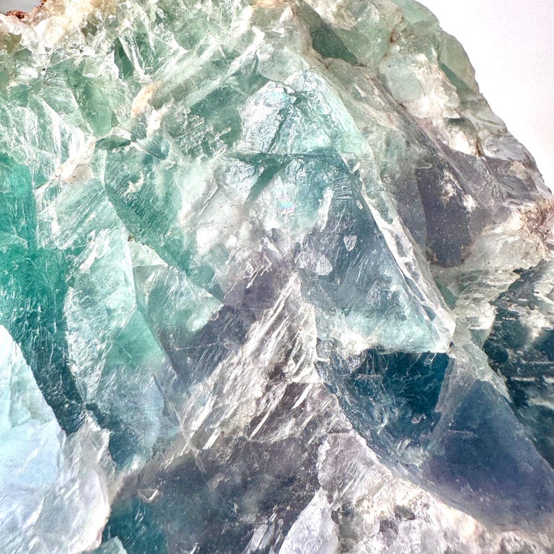May include: A large, rough, green fluorite crystal with a variety of shades of green and white. The crystal has a natural, raw look.