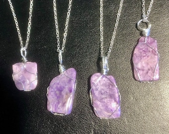 May include: Five silver necklaces with purple amethyst stone pendants. Each pendant is wrapped in silver wire and has a unique shape.