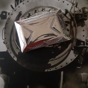 May include: A silver rectangular box with an intricate engraved design. The box has a hinged lid and a small latch.