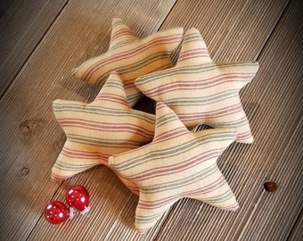 May include: Four striped fabric star-shaped pillows in shades of beige, green, and red, arranged on a wooden surface. Two small red ornaments are in the foreground.