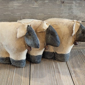 May include: Two handmade fabric sheep with black and white accents and bells. The sheep are made of a beige fabric and have a rustic, farmhouse style.