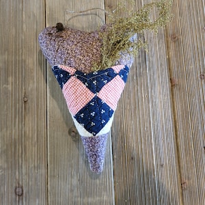 May include: A purple and white heart-shaped fabric pouch with a pink and blue quilted design. The pouch is filled with dried flowers and has a loop for hanging.