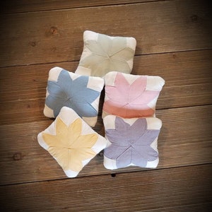 May include: Five fabric flower-shaped pillows in various colors, including light green, blue, pink, yellow, and purple. The pillows are arranged in a semi-circle on a wooden surface.