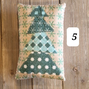 K&ouml;nnte beinhalten: Ein gestepptes Kissen in Form eines Weihnachtsbaums. Das Kissen ist aus beigefarbenem Stoff mit gr&uuml;nem, blauem und wei&szlig;em Patchworkstoff. Das Kissen ist mit Schneeflocken und Sternen verziert.