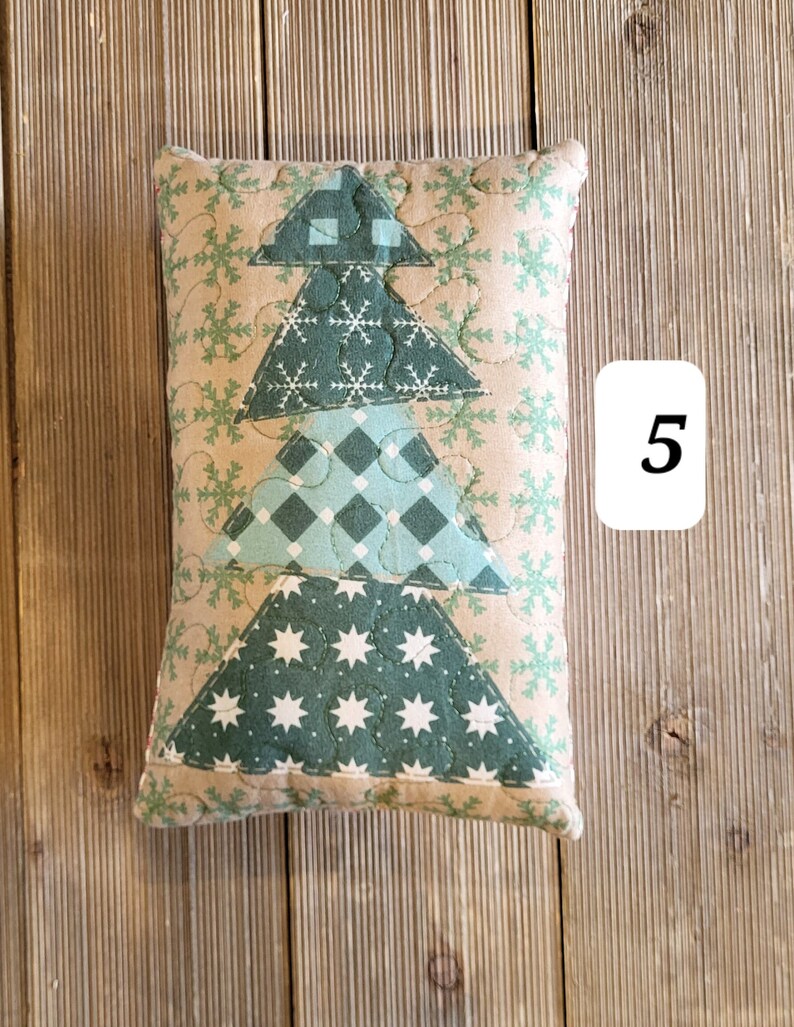 K&ouml;nnte beinhalten: Ein gestepptes Kissen in Form eines Weihnachtsbaums. Das Kissen ist aus beigefarbenem Stoff mit gr&uuml;nem, blauem und wei&szlig;em Patchworkstoff. Das Kissen ist mit Schneeflocken und Sternen verziert.