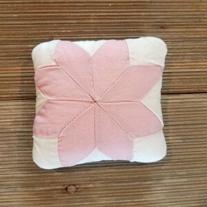 May include: A pink and white patchwork pillow with a starburst design. The pillow is made of soft fabric and has a subtle sheen.