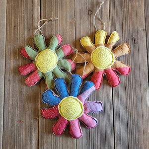 May include: Three handmade fabric flower ornaments with yellow centers and different colored petals. The flowers are hanging from twine.
