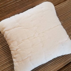 May include: A white quilted pillow with a star-shaped design. The pillow is made of a soft, textured fabric.