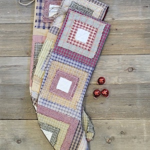 May include: A patchwork Christmas stocking with a rustic design. The stocking is made of different fabrics in shades of red, blue, green, and beige. It has a white fabric lining and a frayed edge.
