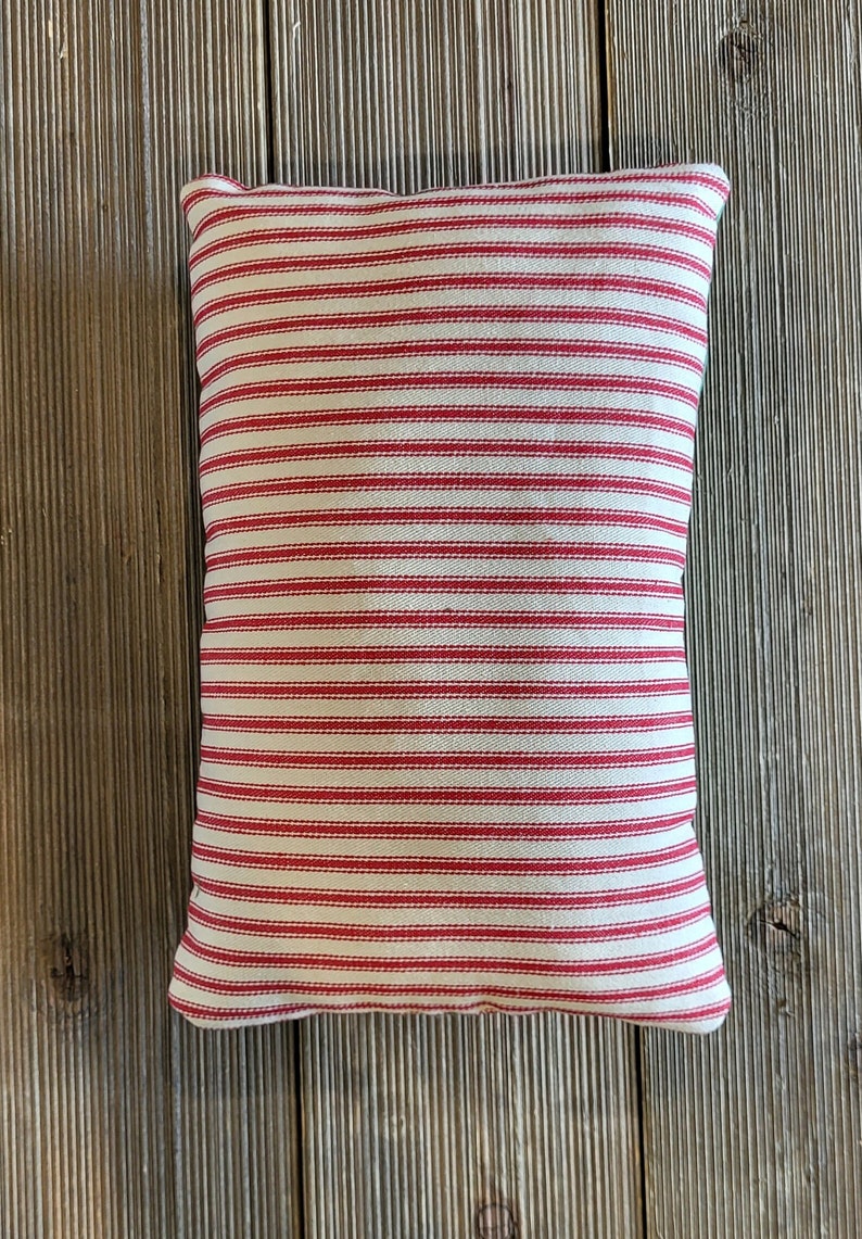 K&ouml;nnte beinhalten: Ein rot-wei&szlig; gestreiftes Kissen aus weichem, strukturiertem Stoff. Das Kissen ist rechteckig und hat ein schlichtes Design.