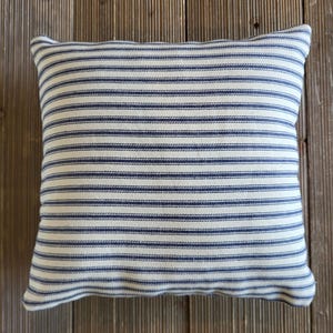 May include: A white and blue striped throw pillow with a subtle texture. The pillow is made of a soft, woven fabric and has a square shape.