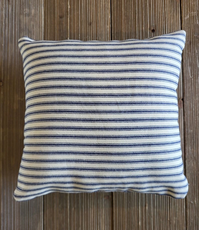 May include: A white and blue striped throw pillow with a subtle texture. The pillow is made of a soft, woven fabric and has a square shape.