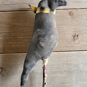 May include: A handcrafted black fabric crow figurine with a yellow and black plaid scarf around its neck. The crow is perched on a small wooden branch, creating a rustic, farmhouse aesthetic. The crow's body has a distressed, vintage look.