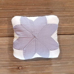 May include: A white and lavender fabric pincushion shaped like a flower with six petals.