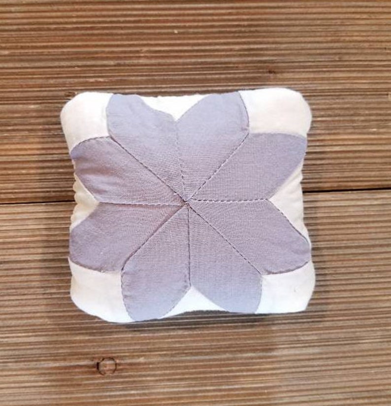 May include: A white and lavender fabric pincushion shaped like a flower with six petals.
