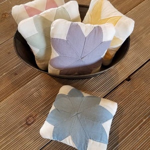 May include: Five small quilted fabric pincushions in a bowl. The pincushions are in shades of pink, green, yellow, purple, and blue. Each pincushion is shaped like a star.