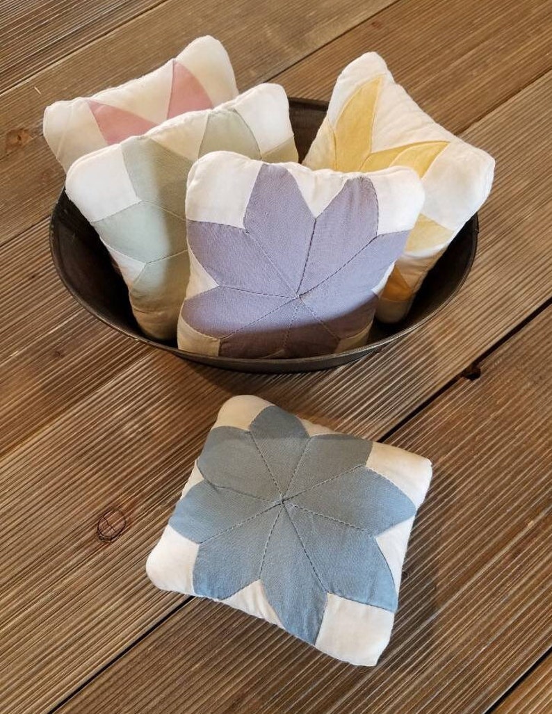 May include: Five small quilted fabric pincushions in a bowl. The pincushions are in shades of pink, green, yellow, purple, and blue. Each pincushion is shaped like a star.