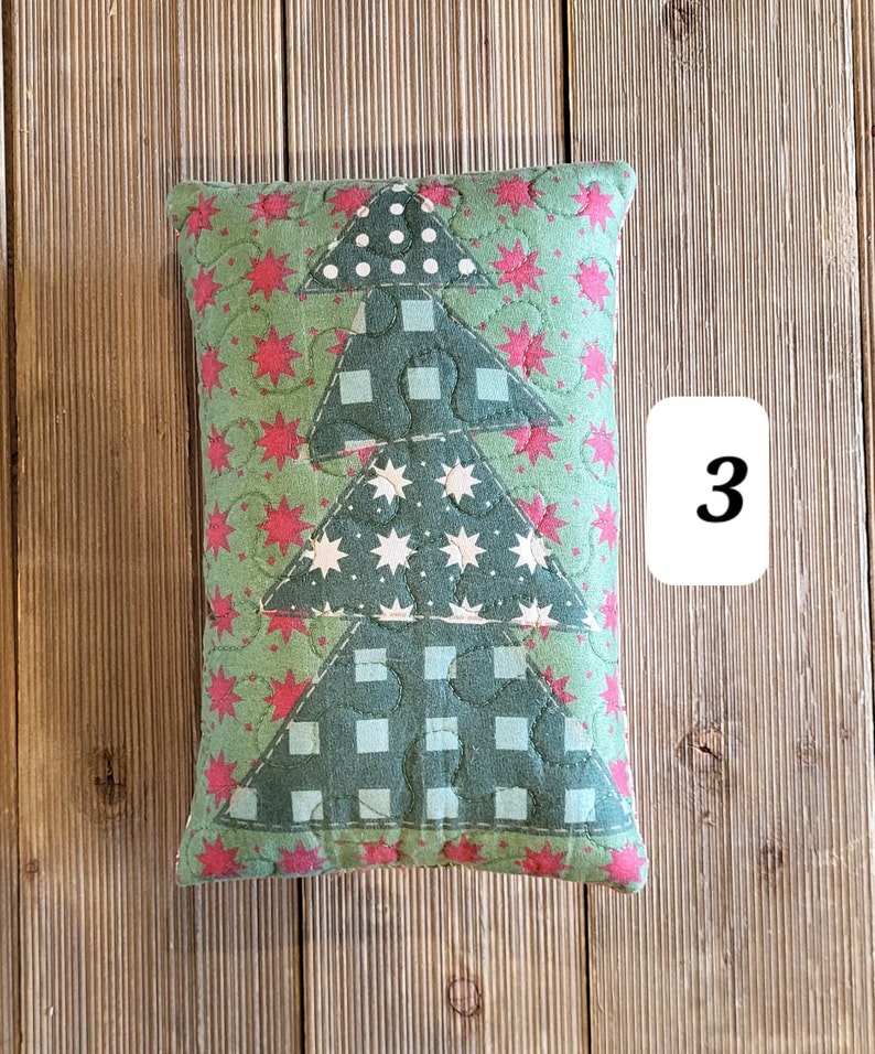 K&ouml;nnte beinhalten: Ein gr&uuml;nes und rotes gestepptes Kissen mit einem Patchwork-Design eines Weihnachtsbaums. Der Baum besteht aus verschiedenen Stoffen mit wei&szlig;en Sternen, roten Sternen und wei&szlig;en Punkten. Das Kissen liegt auf einer Holzoberfl&auml;che.