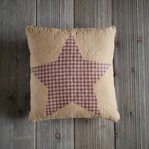 May include: A tan throw pillow with a purple and white gingham star design. The pillow is made of a soft, textured fabric.