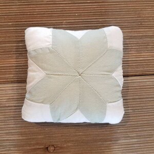 May include: A white and light green pillow with a starburst design. The pillow is made of fabric and has a soft, quilted texture.