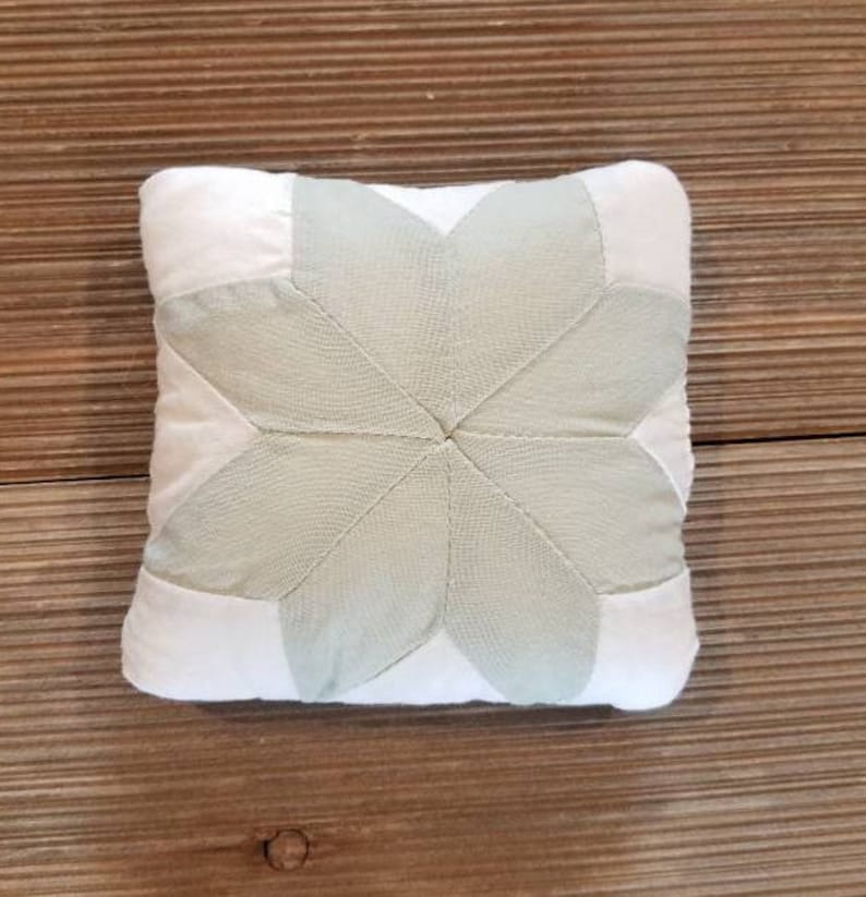 May include: A white and light green pillow with a starburst design. The pillow is made of fabric and has a soft, quilted texture.