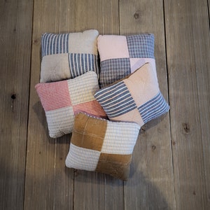 May include: Five patchwork pillows with a variety of colors and patterns, including pink, blue, red, brown, and white. The pillows are arranged in a semi-circle on a wooden surface.