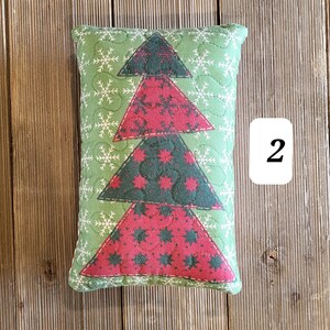 K&ouml;nnte beinhalten: Ein gr&uuml;nes und rotes Weihnachtsbaumkissen mit gestepptem Design. Das Kissen liegt auf einem Holzgrund.