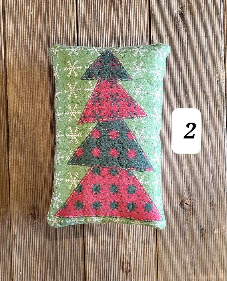 K&ouml;nnte beinhalten: Ein gr&uuml;nes und rotes Weihnachtsbaumkissen mit gestepptem Design. Das Kissen liegt auf einem Holzgrund.