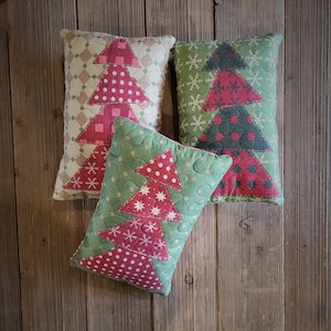 K&ouml;nnte beinhalten: Drei dekorative Kissen mit einem Weihnachtsbaum-Motiv. Die Kissen sind aus Stoff mit einer gesteppten Textur. Die B&auml;ume sind rot, gr&uuml;n und wei&szlig;.