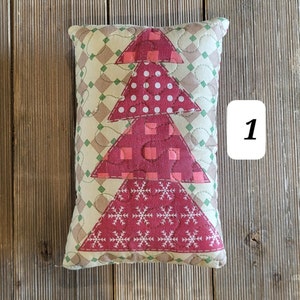 K&ouml;nnte beinhalten: Ein rotes, gr&uuml;nes und wei&szlig;es gestepptes Kissen mit einem Weihnachtsbaum-Motiv. Das Kissen liegt auf einer Holzoberfl&auml;che.