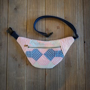 May include: A pink and blue patchwork fanny pack with a zippered pocket and a black adjustable strap.