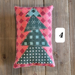 K&ouml;nnte beinhalten: Ein rosa-gr&uuml;nes gestepptes Kissen mit einem Weihnachtsbaum-Motiv. Das Kissen ist mit Schneeflocken, Punkten und Karomustern verziert. Die Zahl "4" ist im Hintergrund sichtbar.