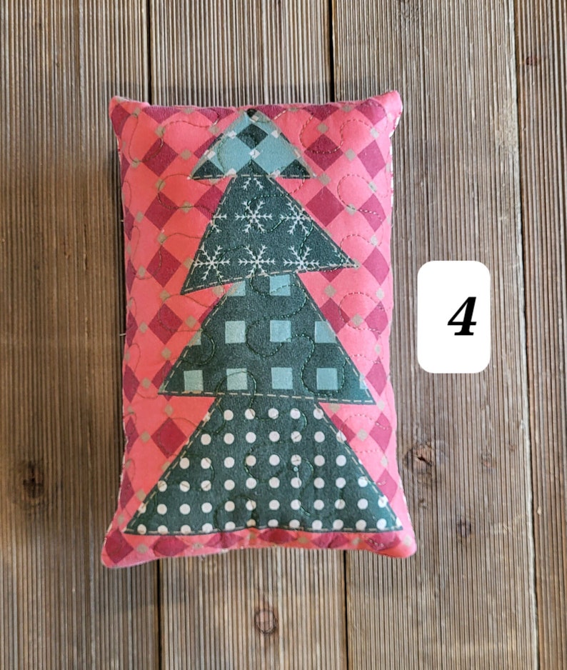 K&ouml;nnte beinhalten: Ein rosa-gr&uuml;nes gestepptes Kissen mit einem Weihnachtsbaum-Motiv. Das Kissen ist mit Schneeflocken, Punkten und Karomustern verziert. Die Zahl "4" ist im Hintergrund sichtbar.
