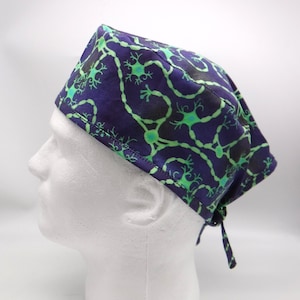 May include: A purple and green patterned surgical scrub hat with a tie at the back. The pattern features a repeating design of green neurons on a purple background.