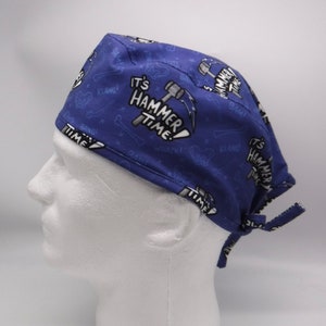 Könnte beinhalten: Blaue chirurgische Mütze mit einem weißen Druck von Hämmern und dem Text "It's Hammer Time!" wiederholt über den gesamten Stoff.