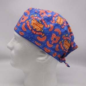 Puede incluir: Gorro quirúrgico azul con un patrón de intestinos naranjas y el texto "Come for the Guts, Stay for the Butts, Colorectal Surgery". El gorro está atado en la parte trasera.