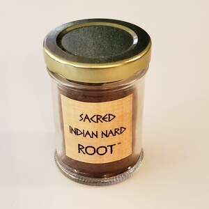 Könnte beinhalten: Ein Glasgefäß mit goldenem Deckel, gefüllt mit braunem Pulver. Das Etikett auf dem Gefäß lautet "Sacred Indian Nard Root".