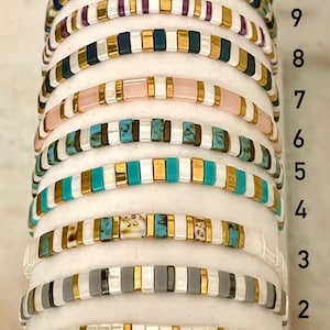 May include: Ten stacked bracelets with different colored beads and gold accents. The bracelets are numbered 1 through 10.