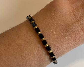May include: A black and gold beaded bracelet with square-shaped beads.